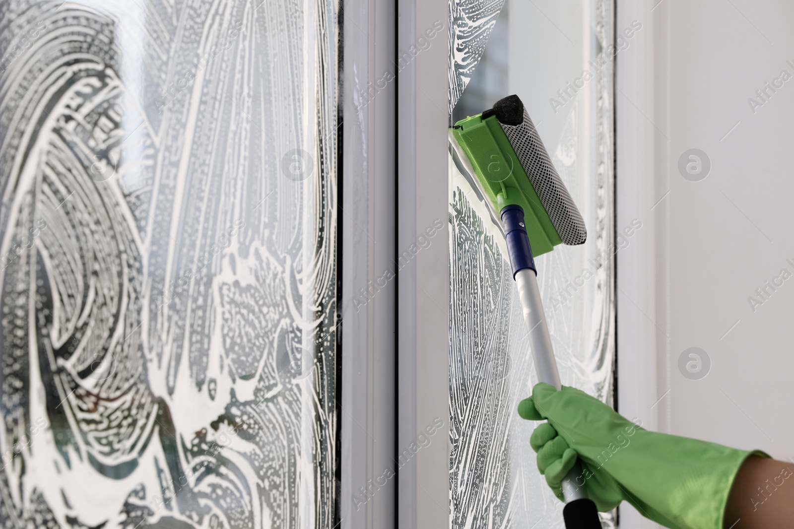 Photo of Woman cleaning window with squeegee indoors, closeup