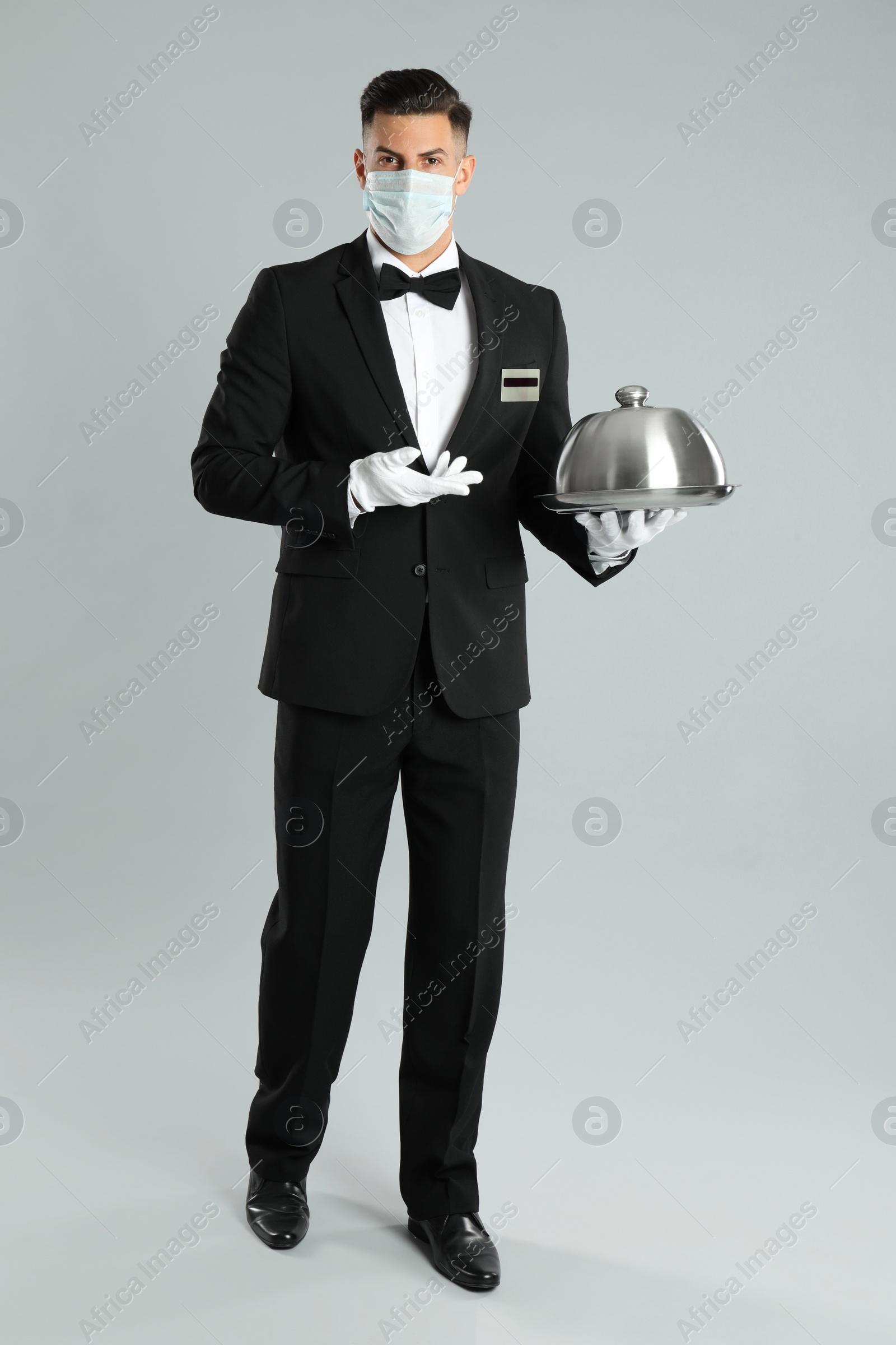Photo of Waiter in medical face mask holding tray on light grey background