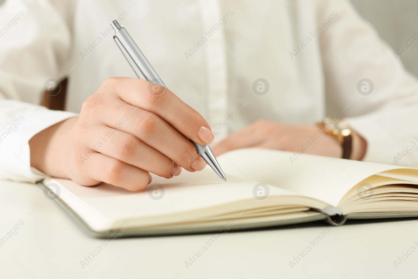 Photo of Woman writing in notebook at white table, closeup