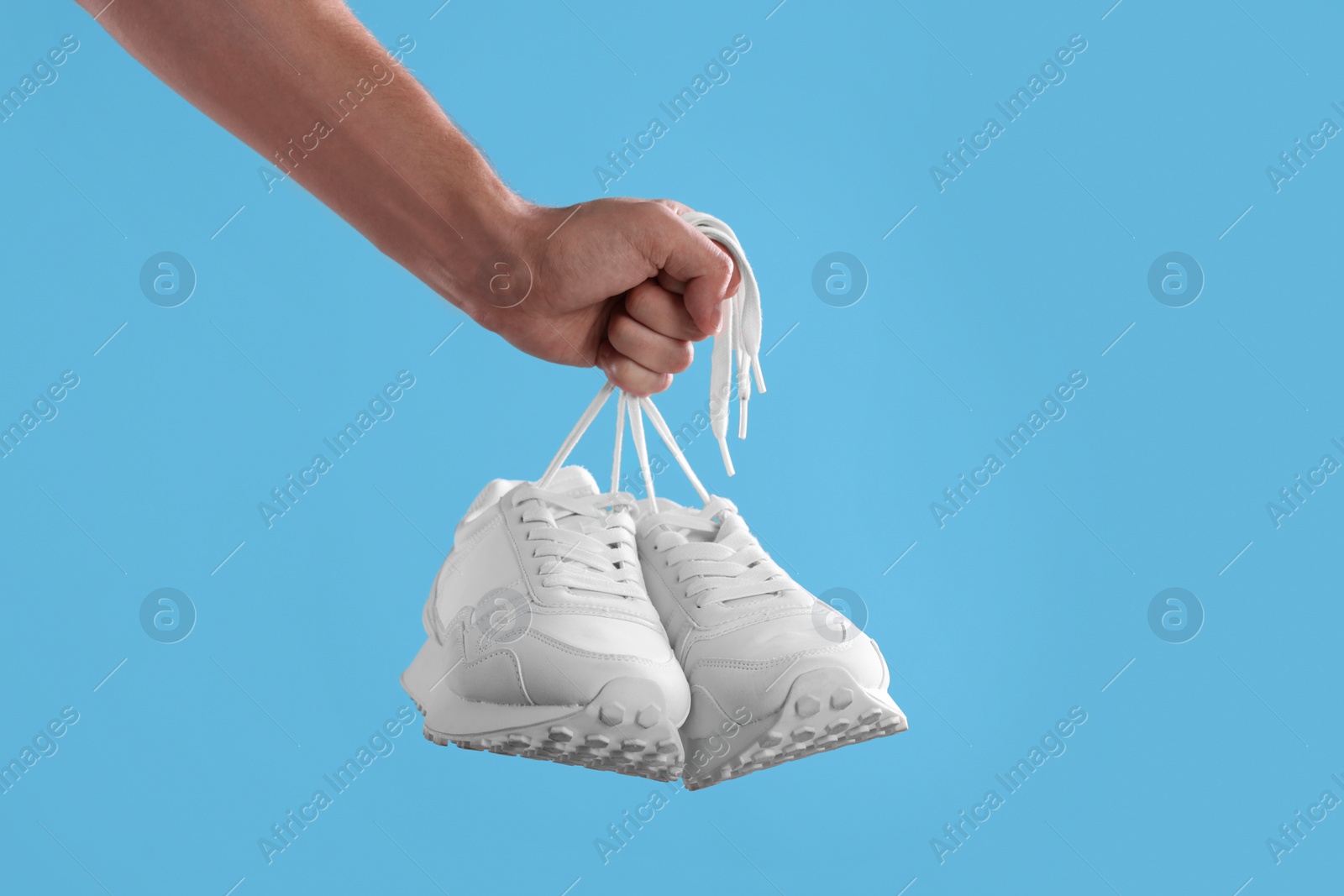 Photo of Man holding stylish sneakers on light blue background, closeup