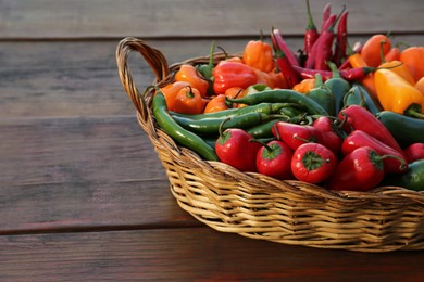 Photo of Wicker basket with many different fresh chilli peppers on wooden table, space for text