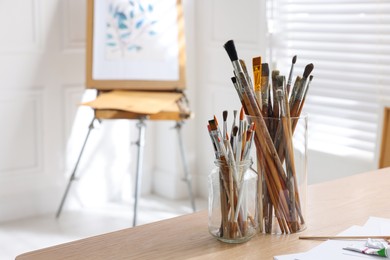 Photo of Holders with different paintbrushes on wooden table in studio, space for text. Artist's workplace
