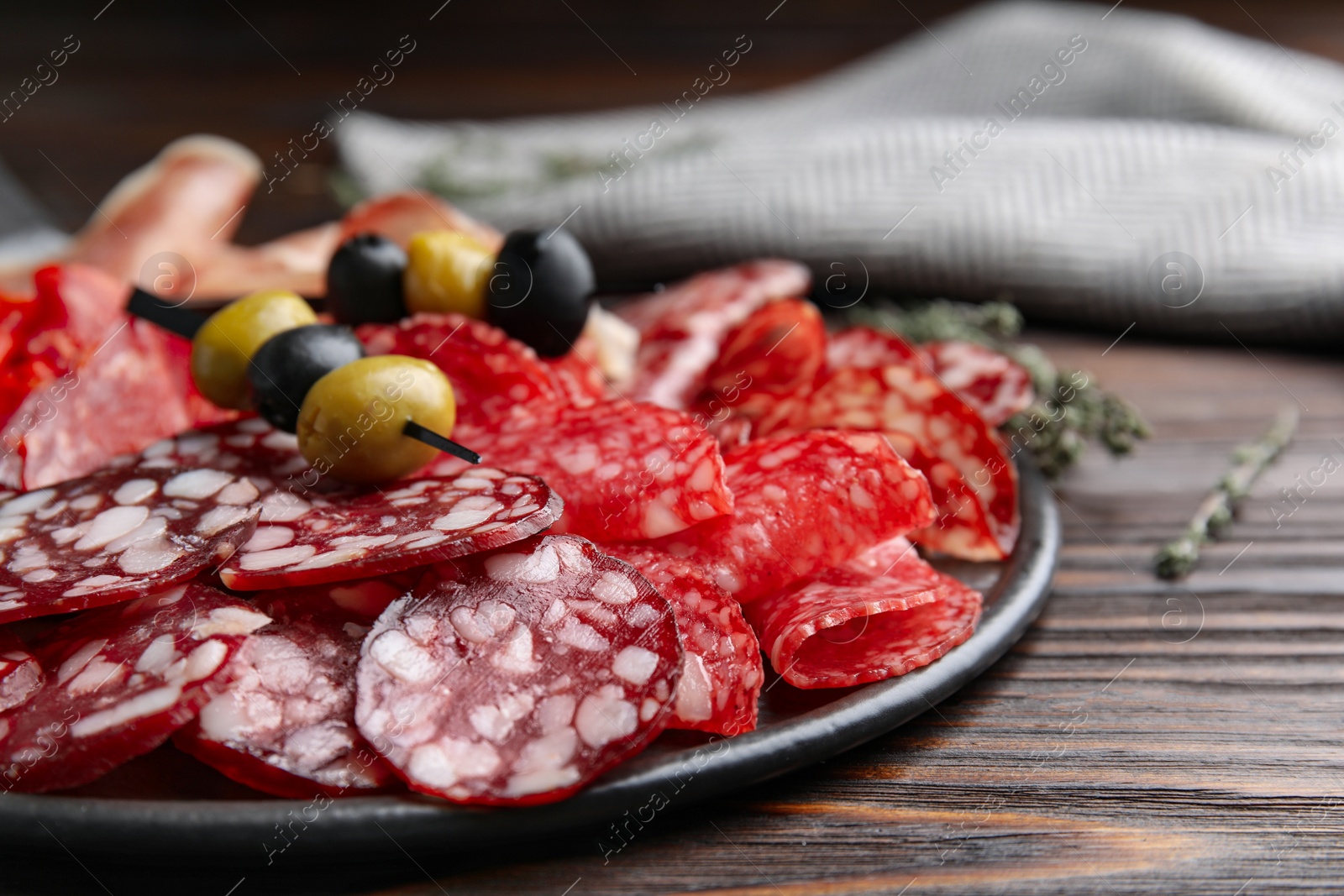 Photo of Tasty salami and other delicacies on wooden table, closeup