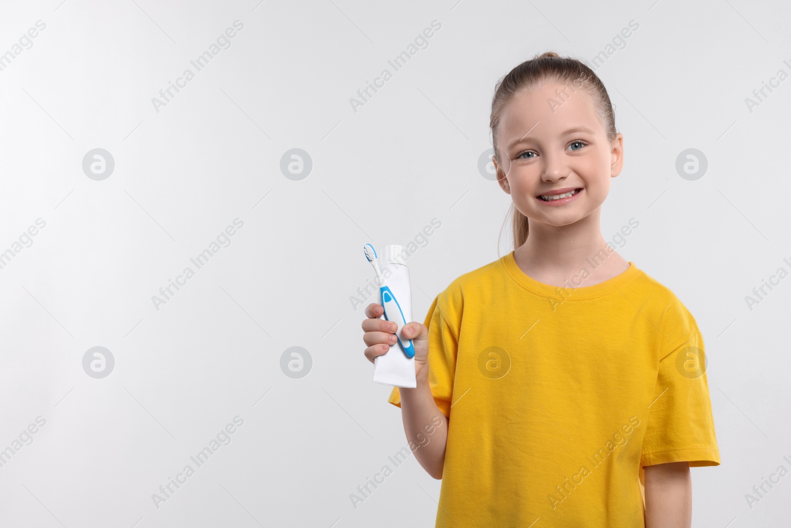 Photo of Happy girl holding toothbrush and tube of toothpaste on white background. Space for text