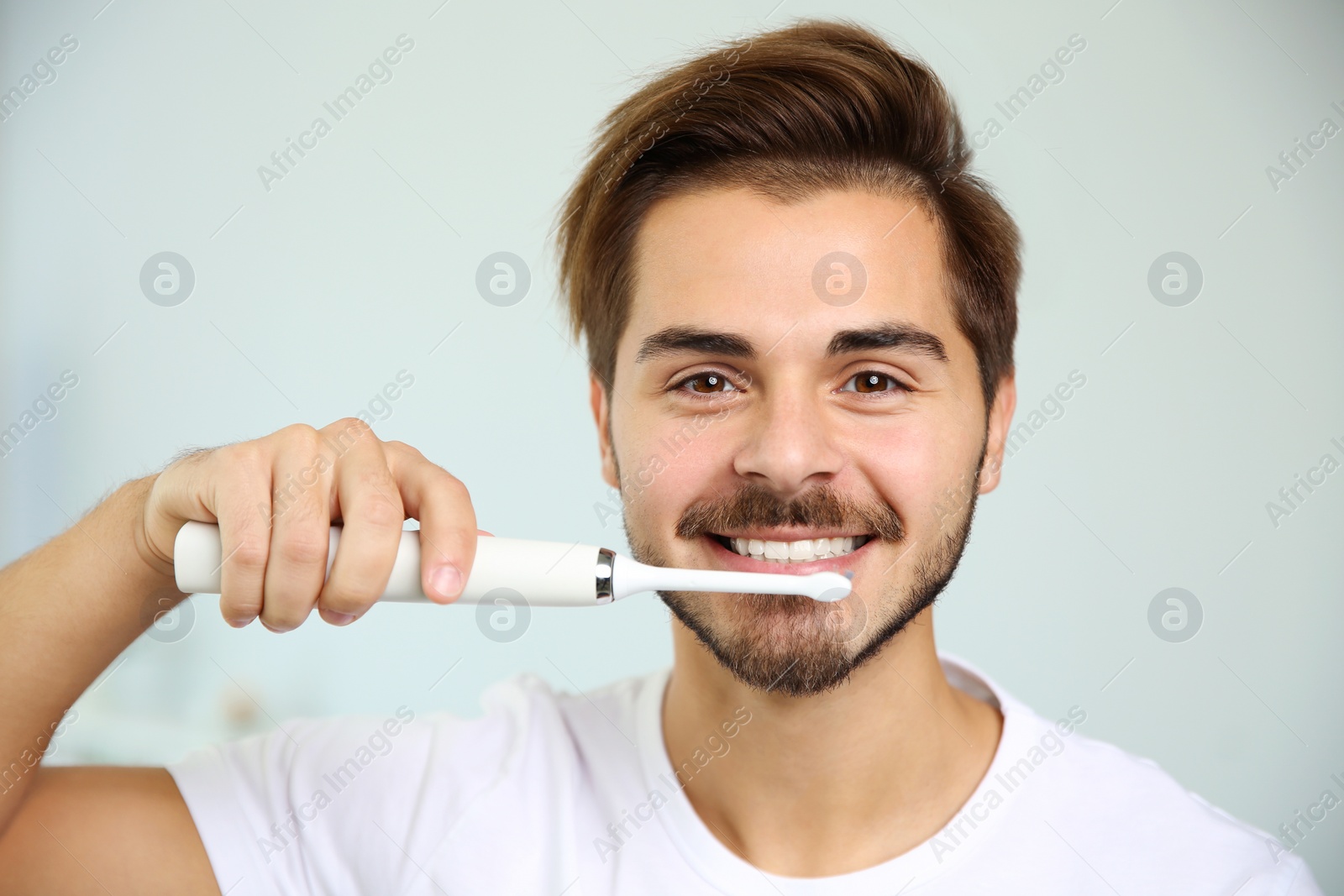 Photo of Portrait of young man with electric toothbrush on blurred background