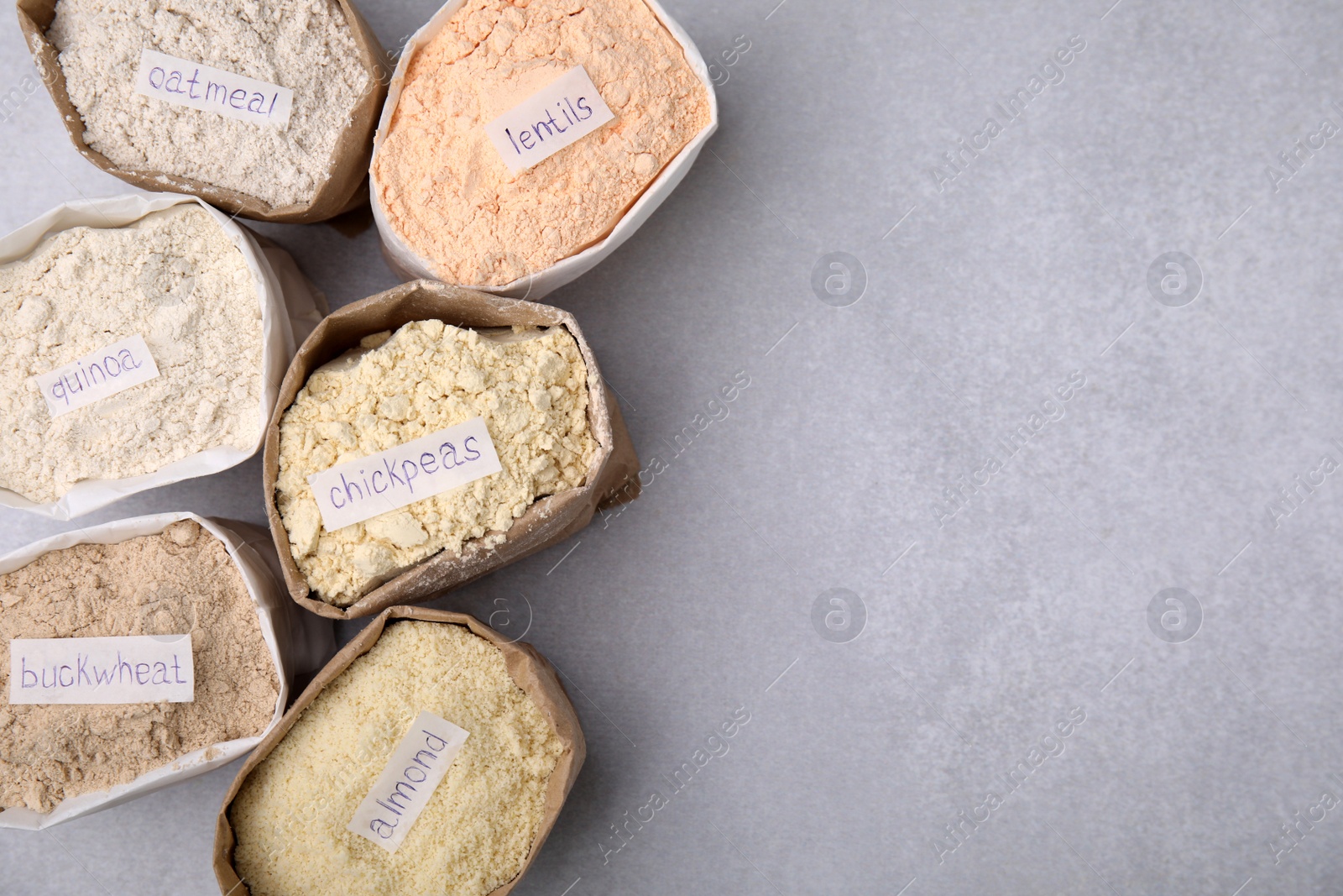 Photo of Sacks with different types of flours on light grey table, flat lay. Space for text