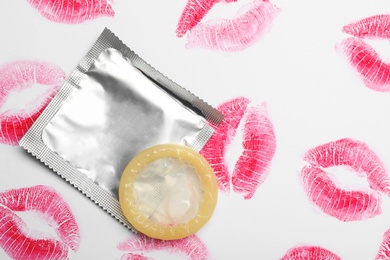 Photo of Condom and lipstick kiss marks on white background, top view. Safe sex