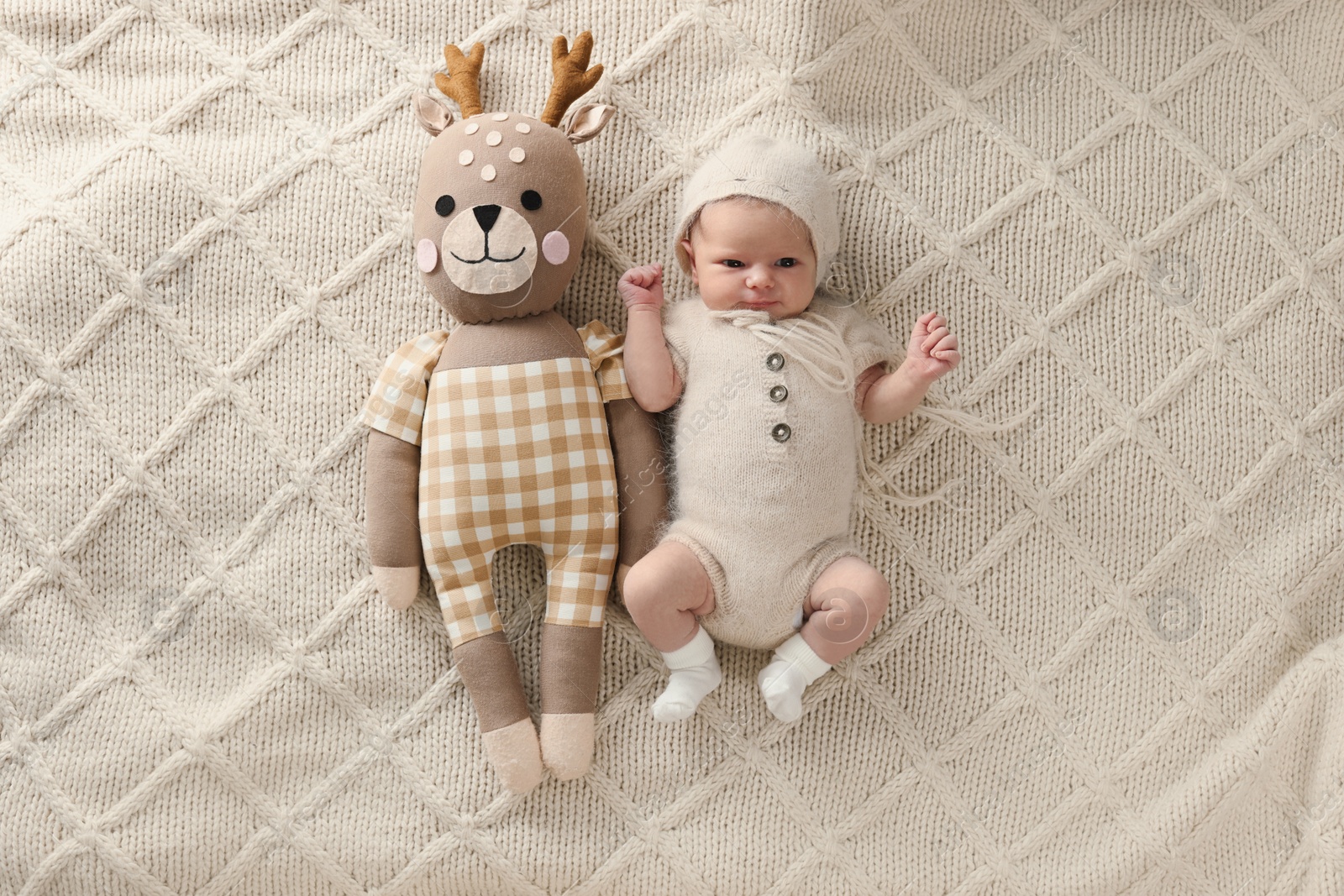 Photo of Adorable little baby with deer toy lying on blanket, top view