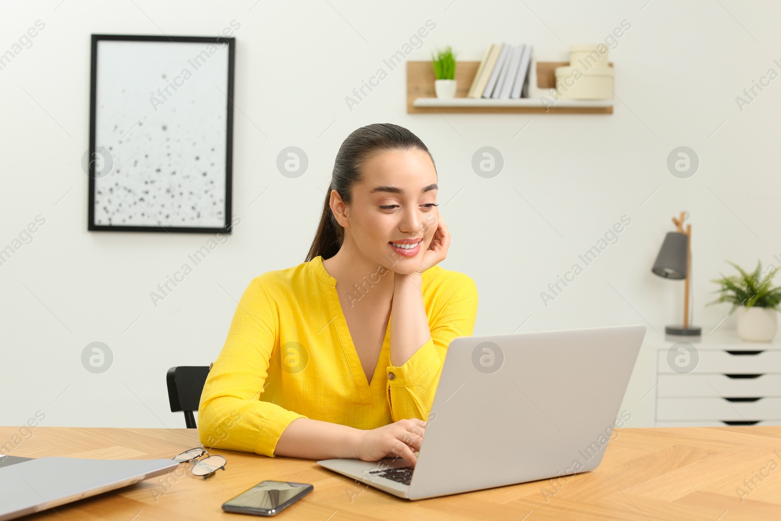 Photo of Home workplace. Happy woman working on laptop at wooden desk in room