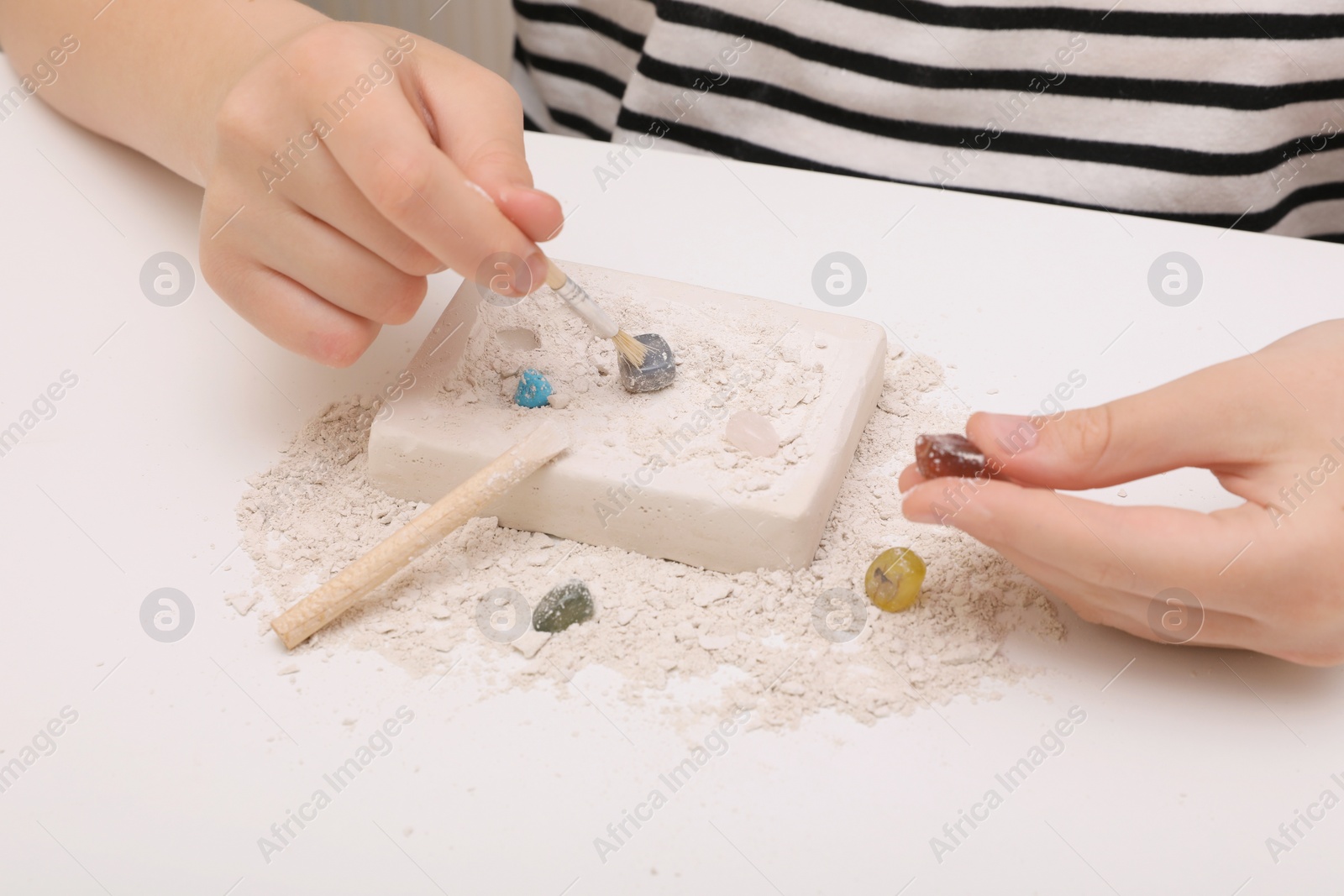 Photo of Child playing with Excavation kit at white table, closeup. Educational toy for motor skills