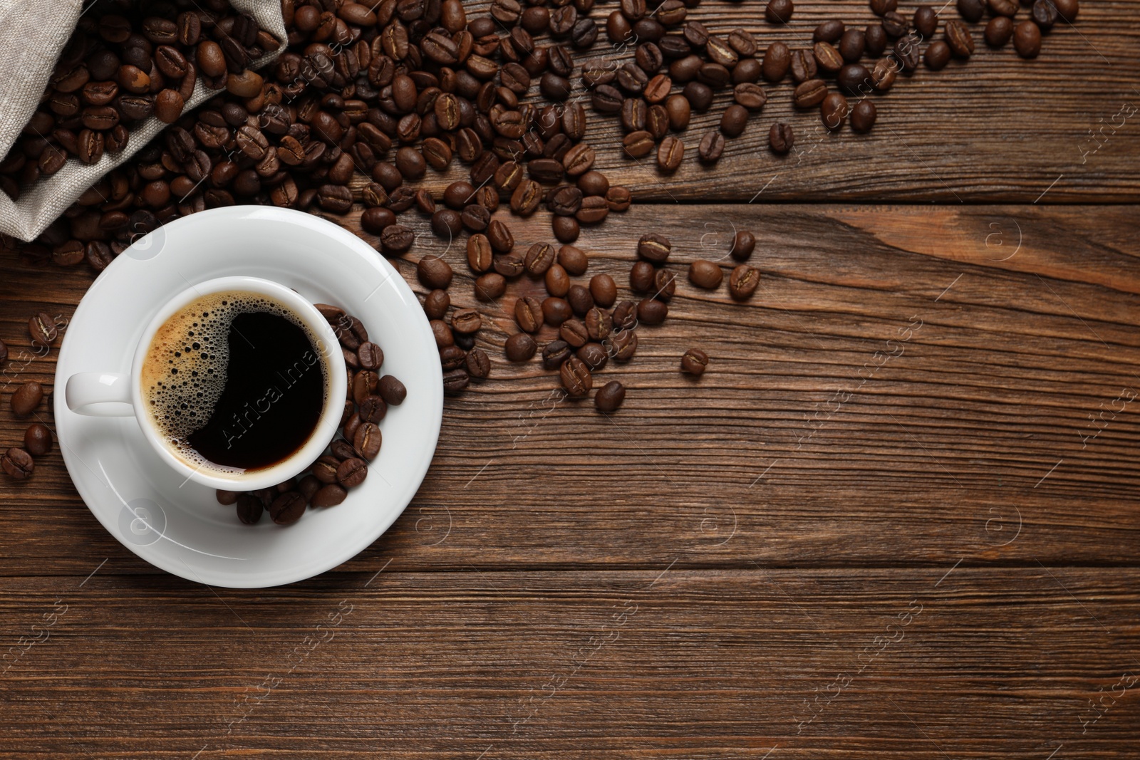 Photo of Cup of aromatic hot coffee and beans on wooden table, flat lay. Space for text