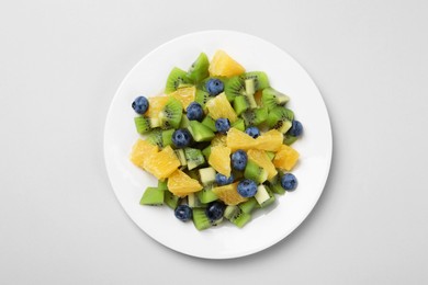 Plate of tasty fruit salad on light grey background, top view