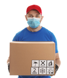 Photo of Courier in mask holding cardboard box with different packaging symbols on white background. Parcel delivery