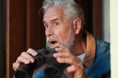 Concept of private life. Curious senior man with binoculars spying on neighbours outdoors