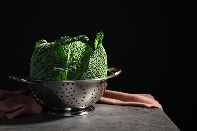 Colander with savoy cabbage on table against black background. Space for text