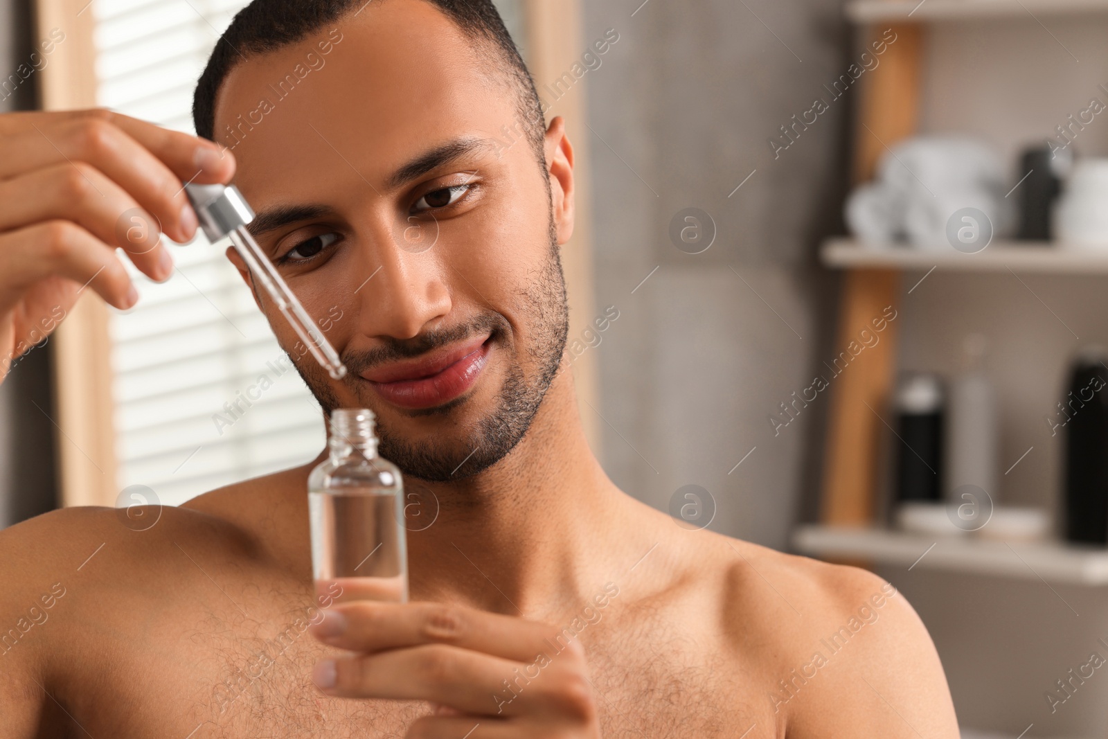 Photo of Handsome man with cosmetic serum in hands in bathroom