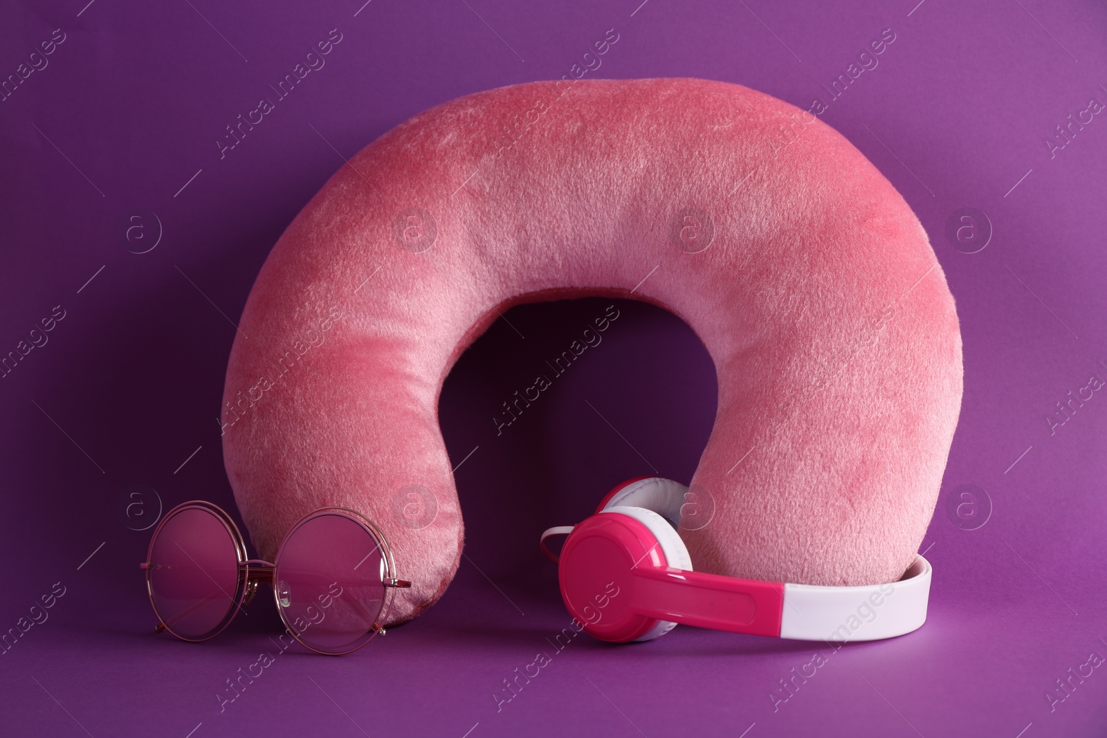 Photo of Pink travel pillow, headphones and sunglasses on violet background