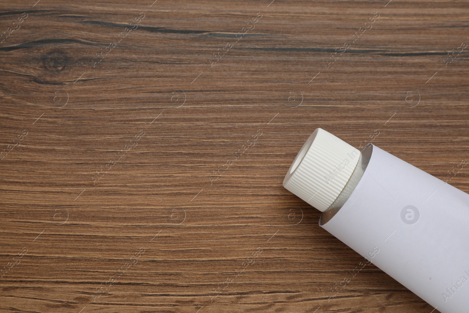 Photo of Blank white tube of ointment on wooden table, top view. Space for text