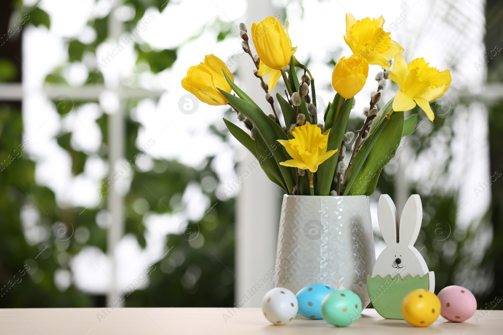 Photo of Festive composition with Easter eggs on table against blurred window, space for text