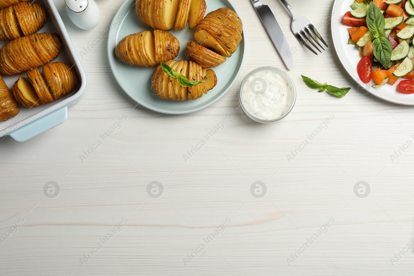 Photo of Delicious homemade Hasselback potatoes served on white wooden table, flat lay. Space for text