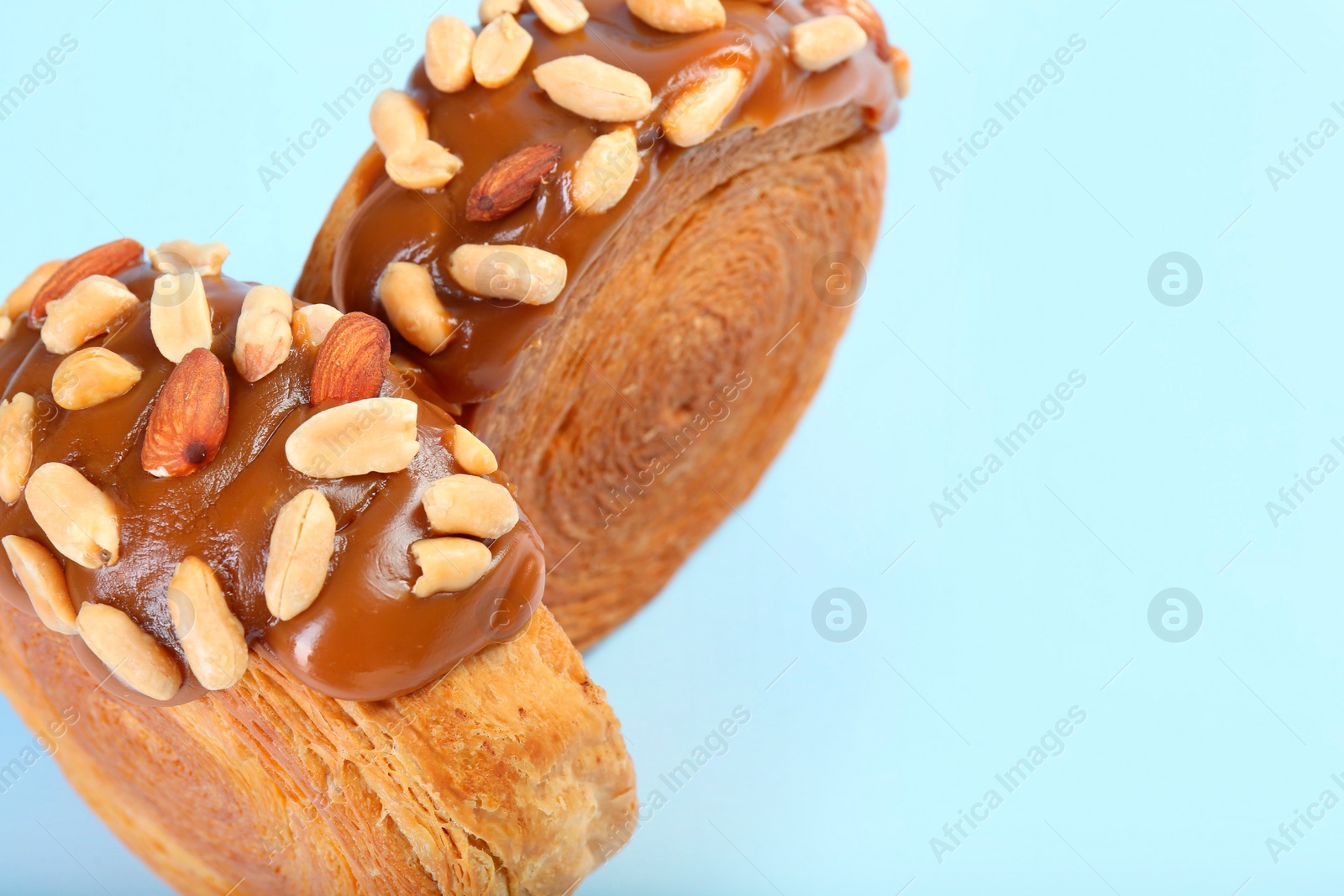 Photo of Tasty puff pastry. Supreme croissants with chocolate paste and nuts on light blue background, closeup. Space for text