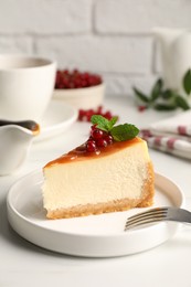 Piece of delicious caramel cheesecake with red currants and mint served on white marble table