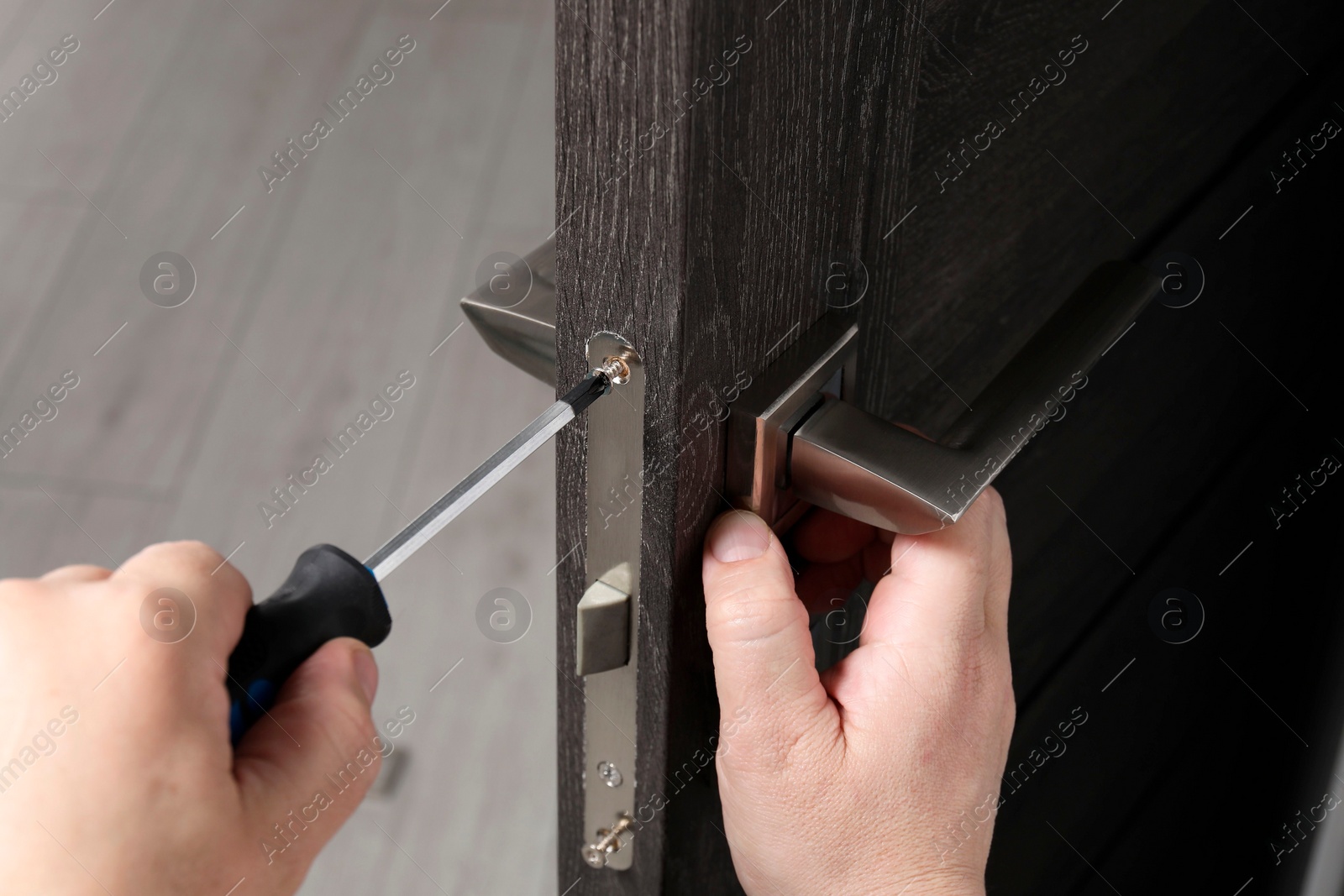 Photo of Handyman with screwdriver repairing door handle indoors, closeup