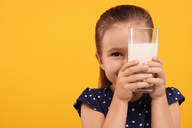 Photo of Cute girl with glass of fresh milk on orange background, space for text