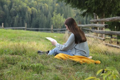 Beautiful young woman drawing with pencil in notepad on green grass