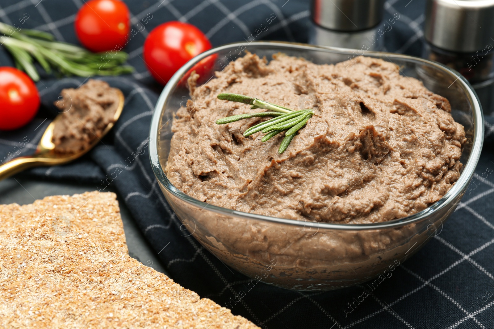 Photo of Tasty liver pate with rosemary in glass bowl and crispy crackers on table, closeup