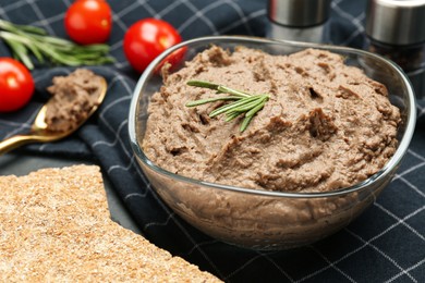 Photo of Tasty liver pate with rosemary in glass bowl and crispy crackers on table, closeup