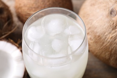 Photo of Glass of coconut water, ice cubes and nuts on wooden table, closeup