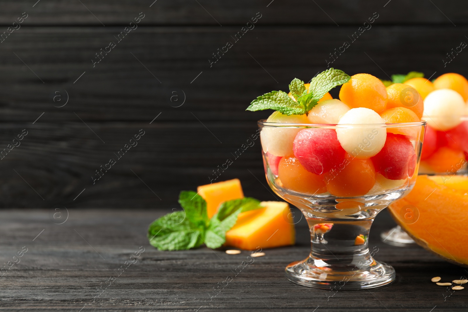 Photo of Melon and watermelon balls with mint in dessert bowl on black wooden table. Space for text