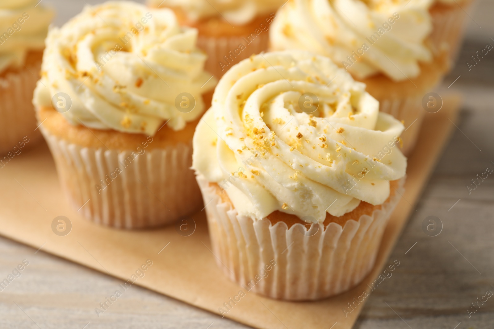 Photo of Tasty cupcake with cream and lemon zest on light wooden table, closeup