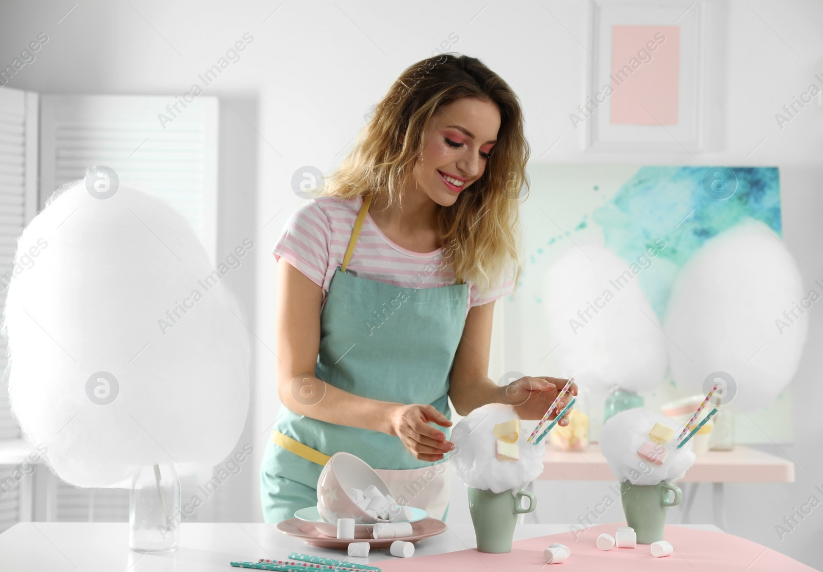 Photo of Young woman with cup of cotton candy dessert at table in room