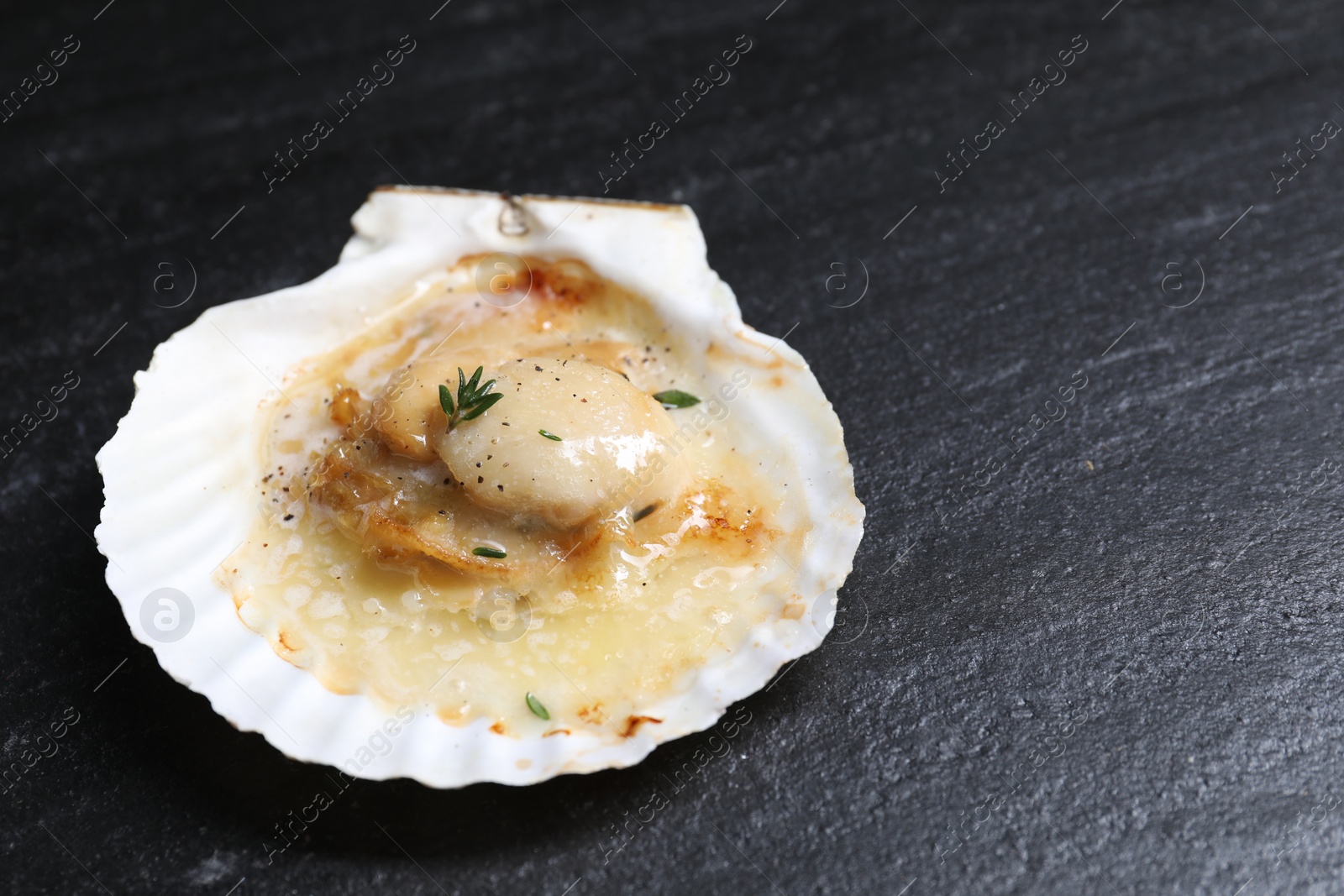 Photo of Fried scallop in shell on black table, closeup. Space for text