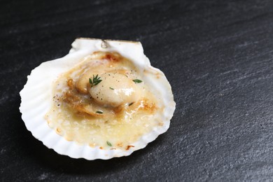 Photo of Fried scallop in shell on black table, closeup. Space for text