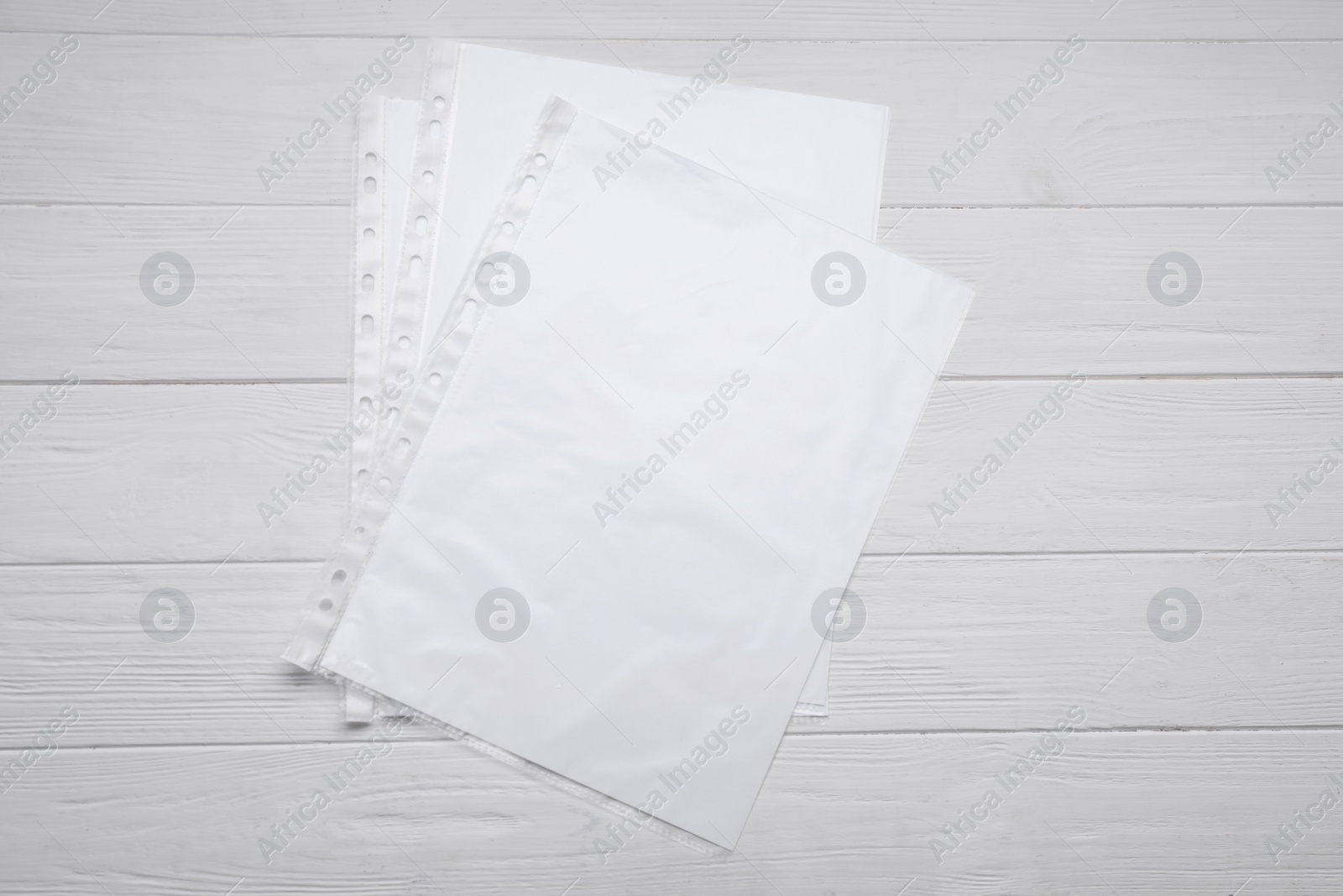 Photo of Punched pockets with paper sheets on white wooden table, flat lay. Space for text