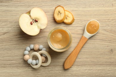 Photo of Tasty baby food in jar, teething toy and ingredients on light wooden table, flat lay
