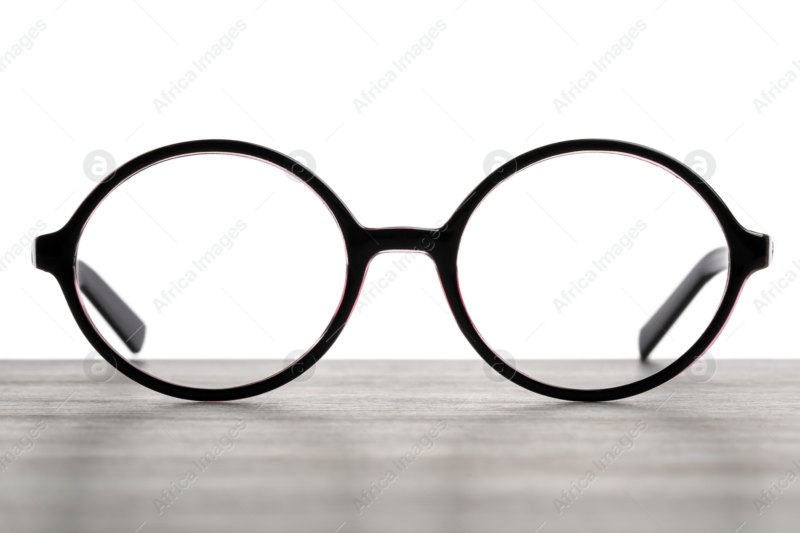 Photo of Stylish glasses with black frame on wooden table against white background