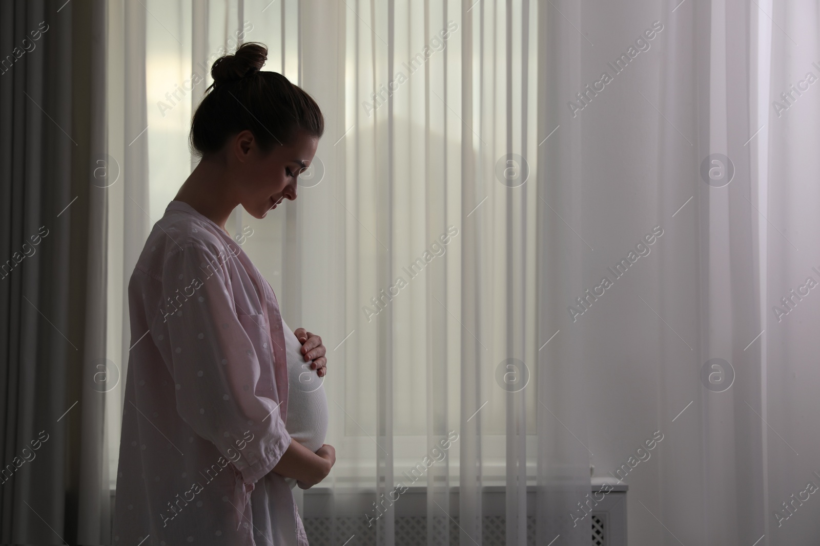 Photo of Young pregnant woman near window at home. Space for text