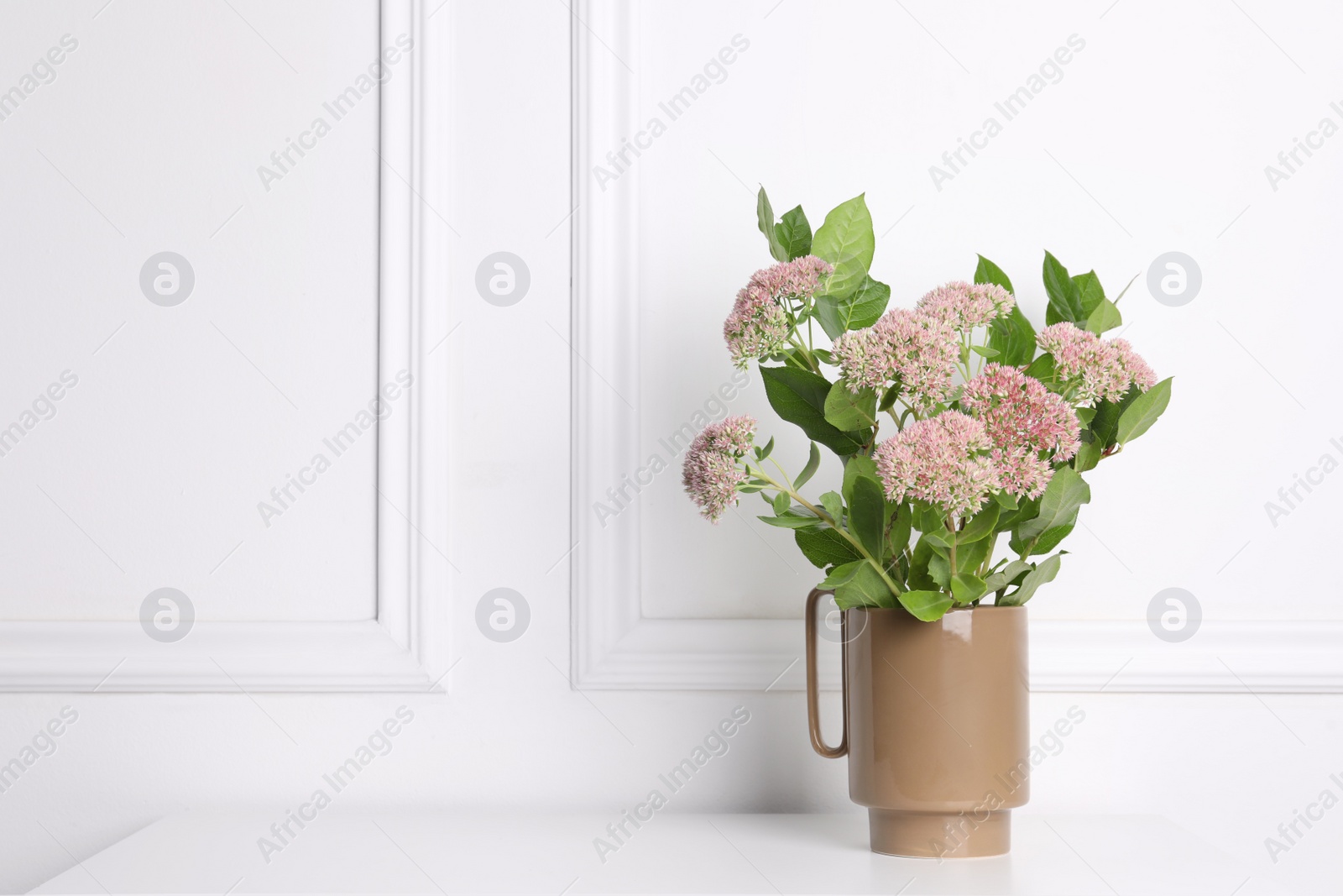 Photo of Stylish ceramic vase with beautiful flowers on table near white wall. Space for text