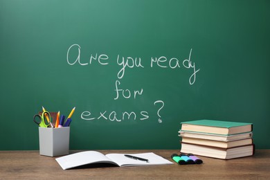 Photo of Different stationery and books on wooden table near chalkboard with phrase Are You Ready For Exams