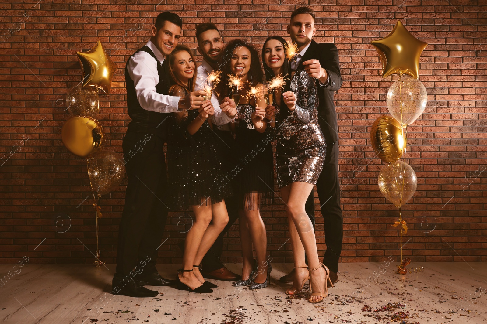 Photo of Happy friends with glasses of sparkling wine and sparklers celebrating New Year indoors