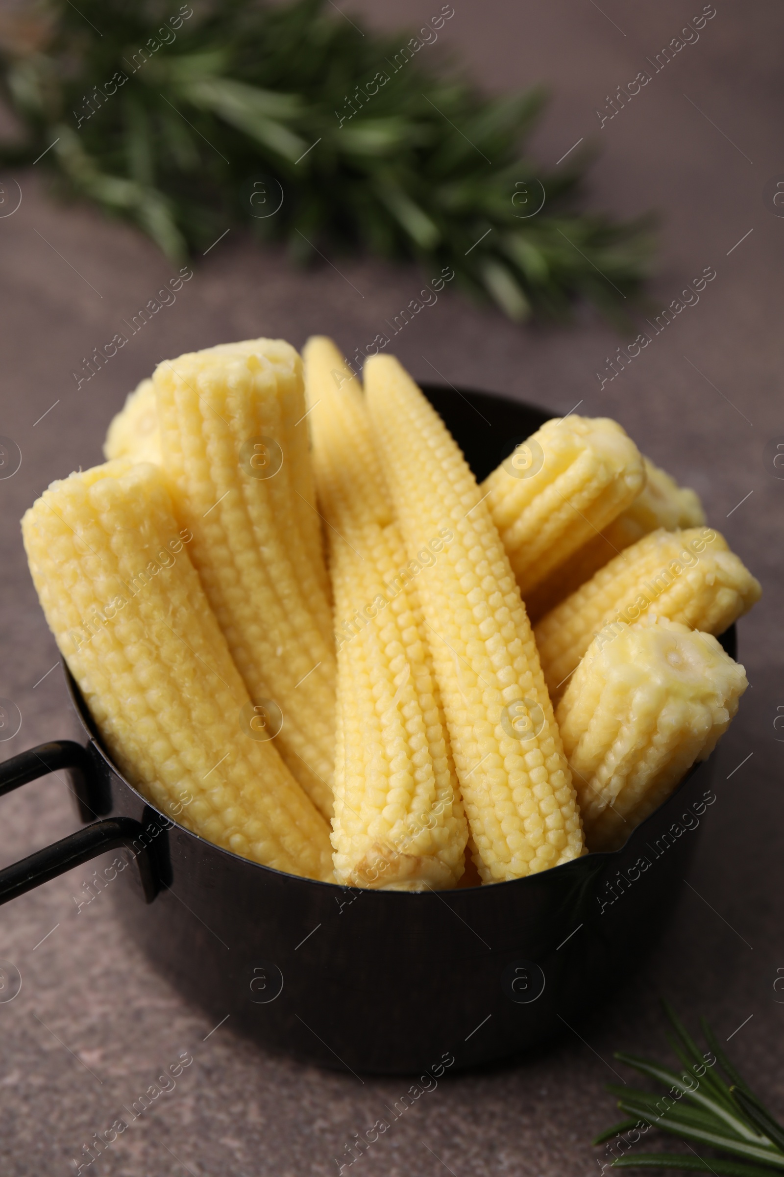 Photo of Tasty fresh yellow baby corns in dish on brown table