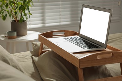 Photo of Wooden tray with modern laptop on bed indoors