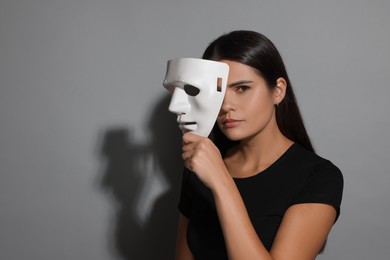 Photo of Multiple personality concept. Woman with mask on grey background, space for text