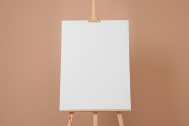 Photo of Wooden easel with blank canvas on beige background