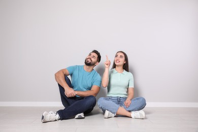 Young couple sitting on floor near light grey wall indoors