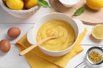 Photo of Delicious lemon curd in bowl, ingredients, spoon and sieve on white wooden table, above view